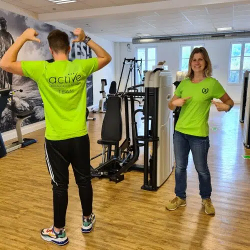 Zwei Personen in neongrünen bedruckten Sportshirts in einem Fitnessstudio