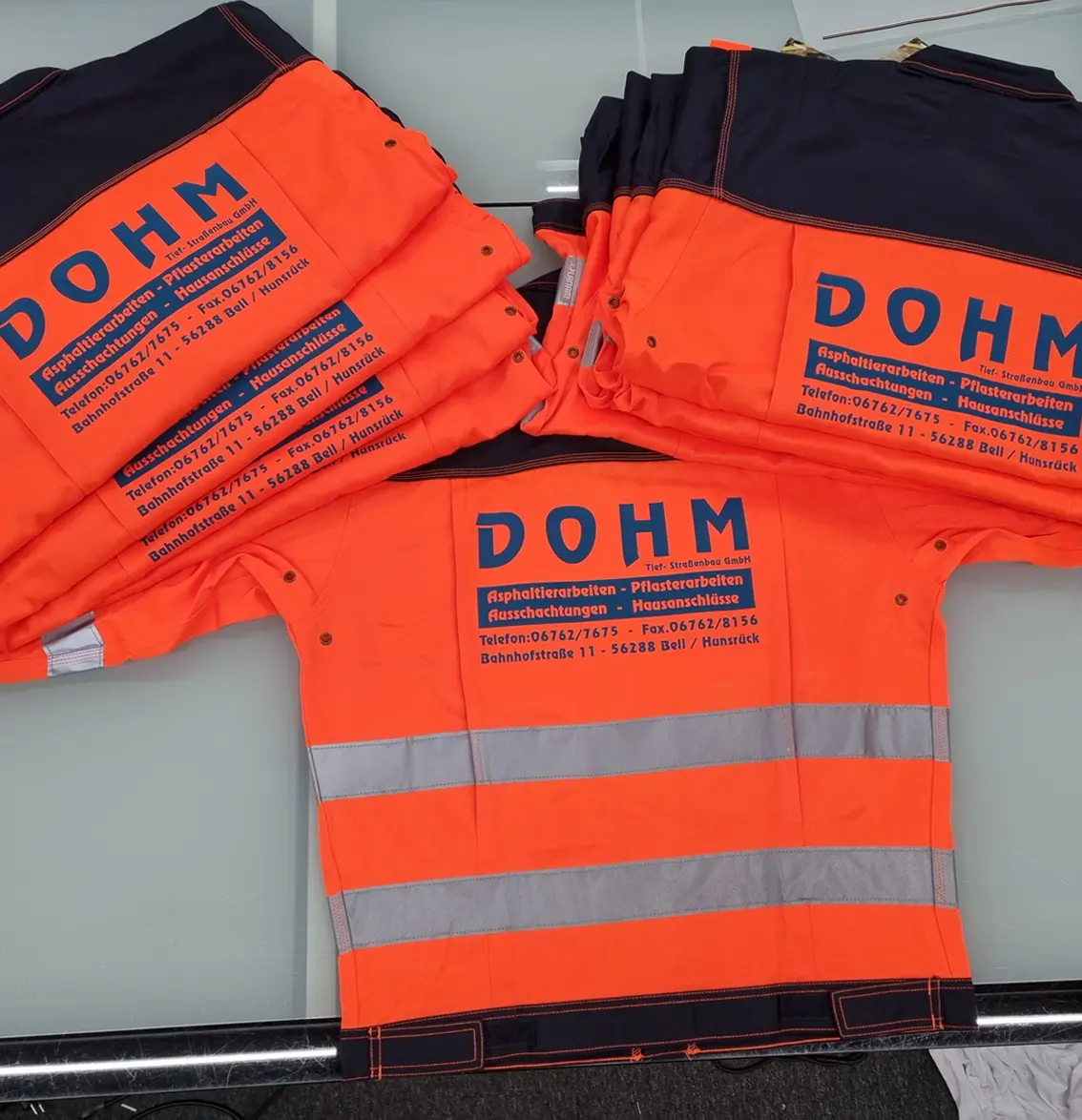 Orange Warnschutzkleidung mit Reflektorstreifen und bedrucktem Firmenlogo Dohm