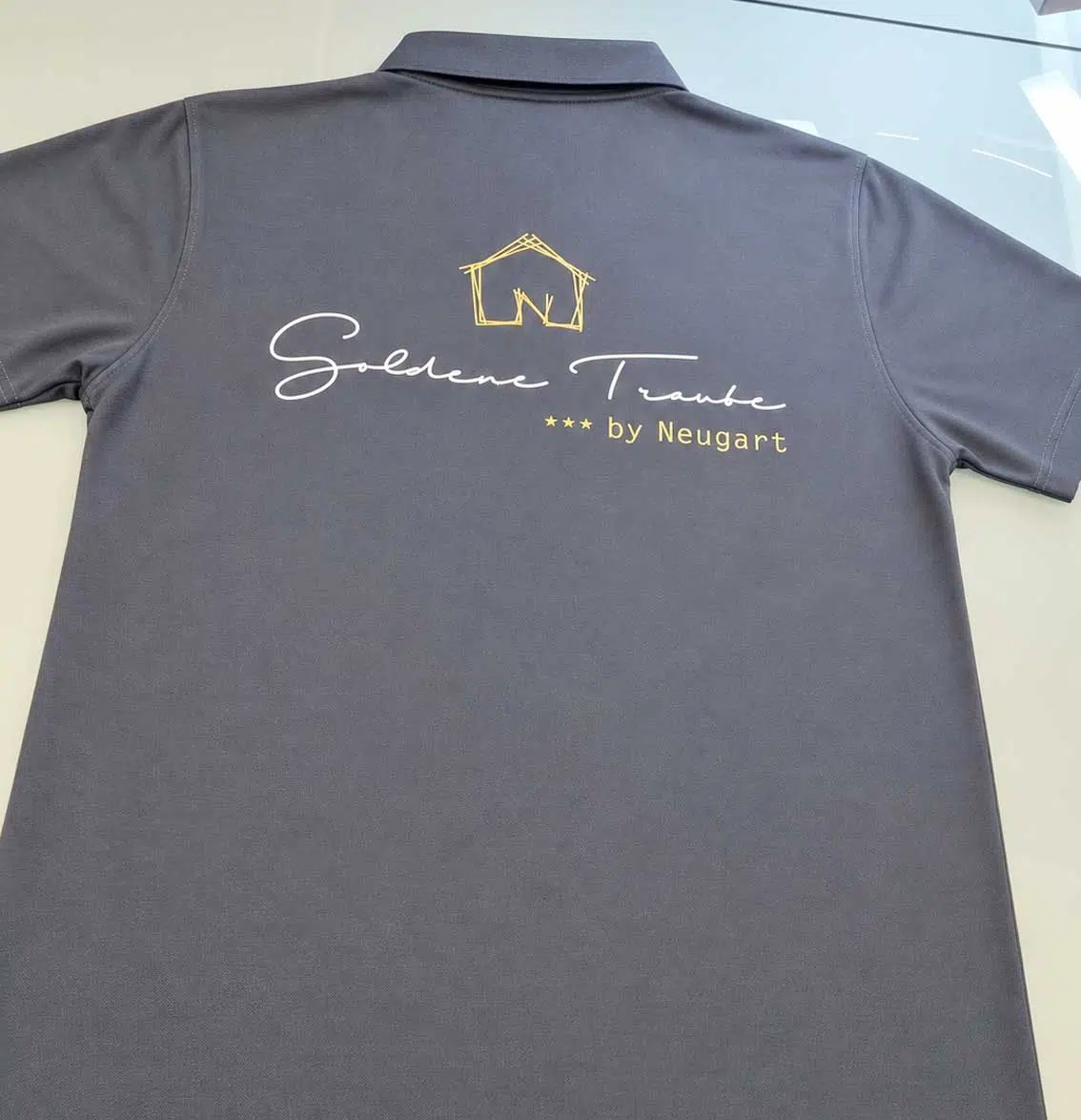 Graues Poloshirt mit goldenem Schriftzug Goldene Traube by Neugart auf dem Rücken